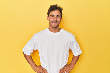 Young Latino man posing on yellow background confident keeping hands on hips.