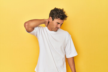 Young Latino man posing on yellow background suffering neck pain due to sedentary lifestyle.