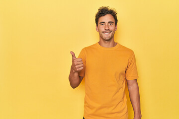 Young Latino man posing on yellow background smiling and raising thumb up