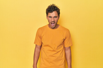 Young Latino man posing on yellow background shouting very angry, rage concept, frustrated.