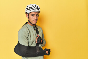 Injured cyclist with bike bag and arm brace on yellow.