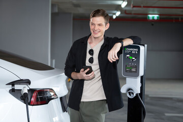 Young man travel with EV electric car to shopping center parking lot charging in downtown city showing urban sustainability lifestyle by green clean rechargeable energy of electric vehicle innards