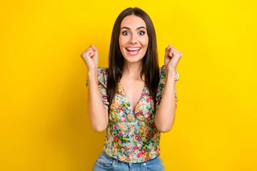 Portrait of impressed funky woman with long hairstyle wear stylish dress clenching fists win betting isolated on yellow color background © deagreez