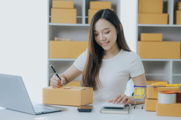 Portrait of a happy Asian woman Starting a small business, SME owner, female entrepreneur Work on receipt boxes and review online orders to prepare boxes for sale to customers. SME online business ide