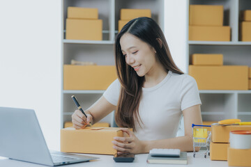 Portrait of a happy Asian woman Starting a small business, SME owner, female entrepreneur Work on receipt boxes and review online orders to prepare boxes for sale to customers. SME online business ide