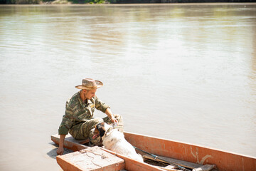 Concentrated fisherman wetting hand in muddy water, while sitting in boat with dog. Side view of...