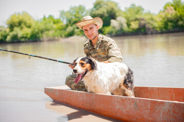 Smiling man in camouflage and hat fishing, while wading in muddy river on old boat. Front view of...