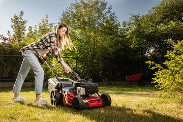 Female gardener working in autumn, cutting grass in backyard. Concept of gardening, work, nature. Housework, gardening and country life. Home garden grass cutting woman mowing with lawn mower.

