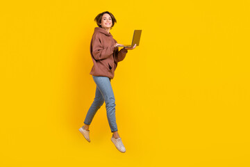 Full size body photo of jumping programmer girl using netbook working remote no limits freelance job isolated on yellow color background