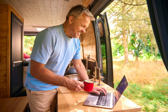 Senior Man On Camping Trip In Countryside Working Inside RV Using Laptop