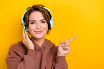 Portrait of young charming woman wear brown sweatshirt listen wireless earphones point finger...