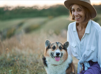 Portrait of funny cute Welsh Corgi dog and laughing charming woman together amidst the scenic lawn