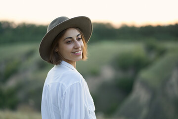 Pretty young woman in hat enjoying the beauty of nature amidst serene hillside landscapes during a captivating sunset