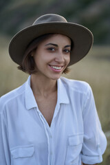 Portrait of beautiful stylish woman with a hat looking to camera in field with dry yellow grass.