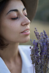 Close up face of beautiful young woman in hat enjoying the aroma of lavender flowers