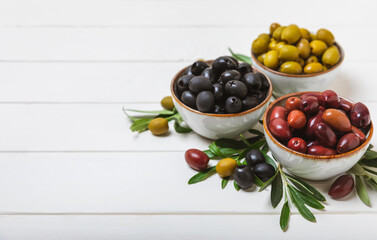 Green and black olives on a textured background. Different types of olives in bowls and olive oil with fresh olive leaves. Delicacy.Mediterranean Kitchen. Copy space.