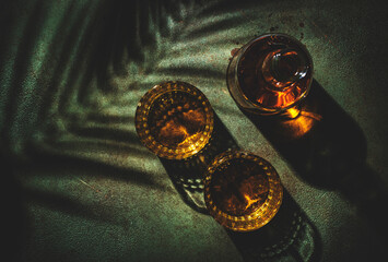 Whiskey, scotch or bourbon in glasses and bottle, green stone background with hard light, shadows...