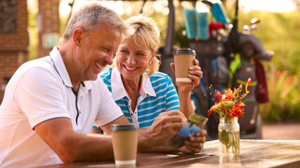 Senior Couple Sitting Having Coffee After Round Of Golf Looking At Score Card Together - Powered by Adobe