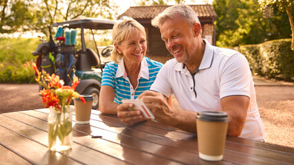 Senior Couple Sitting Having Coffee After Round Of Golf Looking At Score Card Together