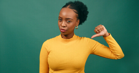 Beautiful young woman gives single thumbs down, green studio background