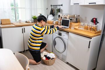 Washing machine and basket with towels in a laundry room. Asian man taking laundry out of washing machine at home