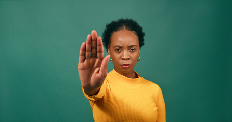 Young Black woman holds up hand saying No, Stop, green studio background
