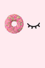 Bunch of donuts and eyelashes made of paper in the shape of a wink. Pink background with copy space.