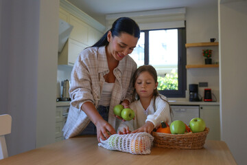 Happy mother and daughter unpacking the groceries from the eco friendly net bag. Mom and her little girl in the kitchen. Close up, copy space, background.