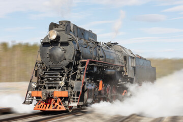 A moving steam locomotive in clouds of smoke in the forest under a cloudy sky