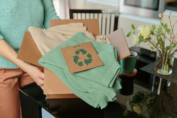Woman packing box with used wardrobe and card with circular economy logo. Reusing, recycling...