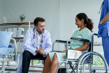 Hispanic female patient sitting in a wheelchair Seeking advice from a Caucasian orthopedic specialist in the examination room. After recovering from an arm injury To prepare for physical therapy - Powered by Adobe