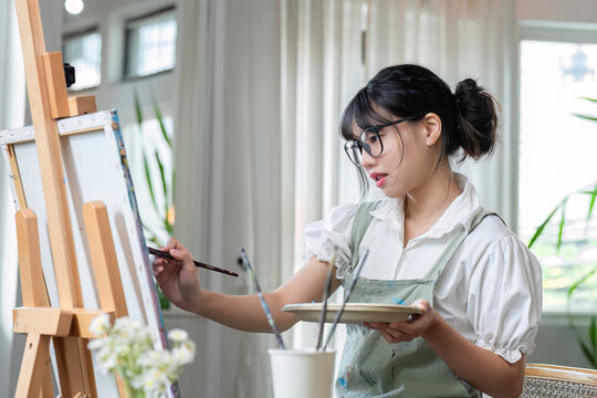 Young female artist works on abstract acrylic painting on canvas in art painting studio.