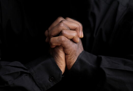 black man praying to god with hands together on black background with people stock image stock photo