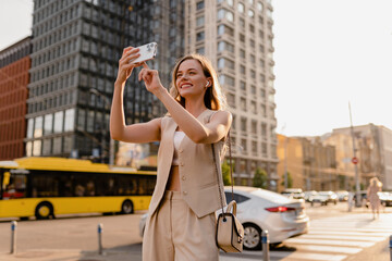 woman walking in sunny city street with phone - obrazy, fototapety, plakaty