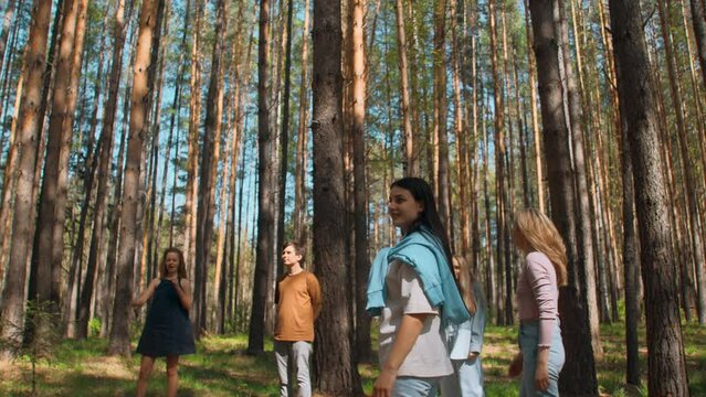 Friends play volleyball in woods. Stock footage. Group of people play ball standing in circle in forest on summer day. Friends relax in nature in sunny weather