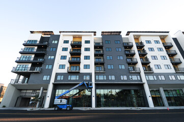 Low-angle view of a new apartment building's upper corner, with windows and balconies, and a blue telescopic boom lift vehicle on the street © Eduardo Barraza