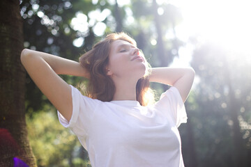 Portrait of happy young woman breathing deep fresh air in the summer forest or park at summer sunny day