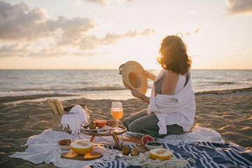 Young woman having beautiful tasty picnic with lemonade, fresh fruits and croissants on a beach at...