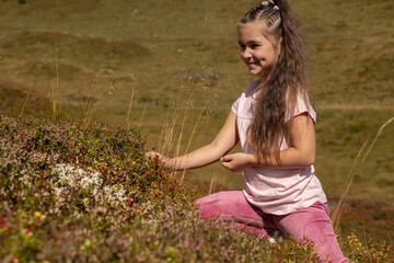 Smiling girl with dimples on her cheeks picking lingonberries on a mountain alpine slope in Austria