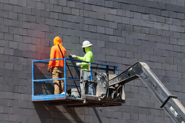 Two construction workers standing on the platform of a telescopic boom lift vehicle and working on...