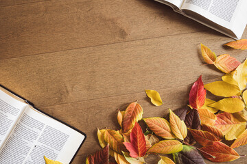 Two bibles and a border of autumn leaves on a light wood table with copy space
