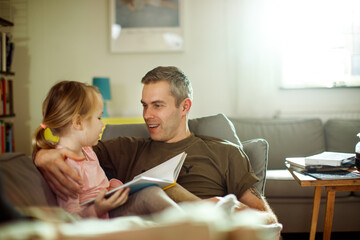 Young father reading with his daughter on the couch after coming back from the army at home