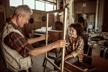 Senior male carpenter showing his grandson a wood frame in a carpentry shop