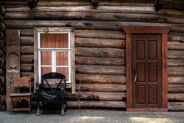 Fototapeta na wymiar Fragment of a log house with a rectangular window in a white frame, a wooden door and a leather chair.