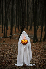 Happy Halloween! Boo! Spooky ghost holding glowing jack o lantern in moody dark autumn forest....