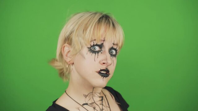 Portrait of a goth girl in black clothes and special makeup on a green background. She looks at the camera and turns her head. Chroma key.
