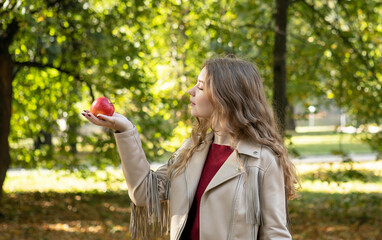 young girl with long blond hair in an autumn park with apple in her hands