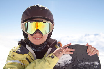 Young woman wearing snowboarding helmet and mask and holding snowboard in hands, snowboarder...