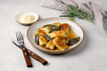Italian homemade gnocchi with potatoes, cheese and sage butter, served in plate on a light table. Italian food. Copy space.