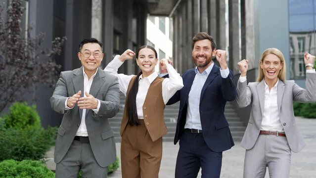 Happy team of business people employees rejoices success. Group employee man and woman managers celebrate a victory looking at camera a city street near a downtown office building. Outside outdoors